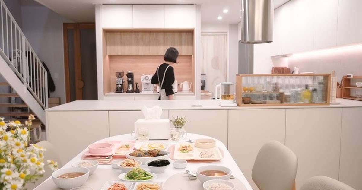 밝은 주방의 식탁에 여러 가지 반찬과 국이 차려져 있고 안쪽에 한 사람이 서 있다