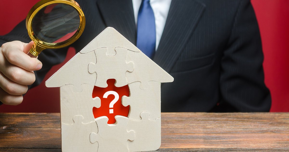 퍼즐로 만든 집 모형에서 빠진 한 조각을 정장 차림의 사람이 돋보기로 들여다보고 있다