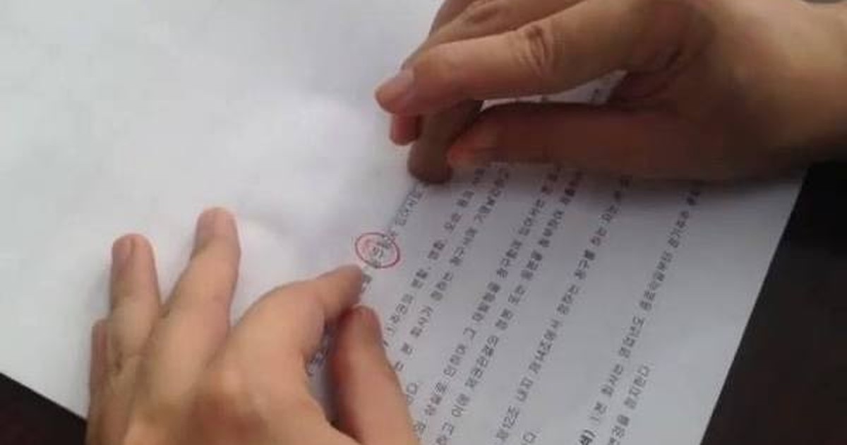 붉은 도장이 찍힌 한글 서류 위를 두 손이 짚고 있다